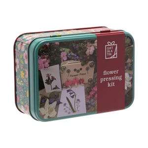 Könnte beinhalten: Eine rechteckige Dose mit floralem Muster und türkisfarbenem Rand. Die Dose enthält ein Blumenpress-Set mit dem Schriftzug "flower pressing kit" auf einem roten Etikett. Im Inneren befinden sich gepresste Blumen und eine kleine Blumenpresse.
