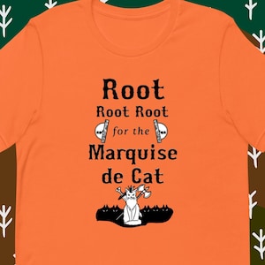 May include: Orange t-shirt with black text that reads "Root Root Root for the Marquise de Cat". A black and white illustration of a cat wearing a crown and holding a sword and axe is below the text.