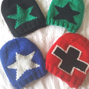Puede incluir: Cuatro gorros de punto con diferentes fondos de colores y diseños de estrellas o cruces. Los gorros son negros con una estrella verde, verdes con una estrella negra, azules con una estrella blanca y rojos con una cruz negra.