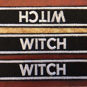 Op de afbeelding: Drie zwarte stoffen patches met witte geborduurde tekst. De bovenste patch staat "WITCH" achterstevoren. De onderste twee patches staan "WITCH" in de juiste richting.