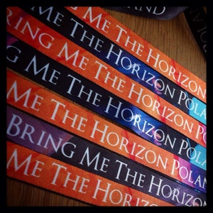 Puede incluir: Un montón de pulseras naranjas y negras con el texto "Bring Me The Horizon" impreso en ellas.