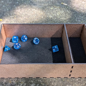 May include: A wooden box with a divider, lined with black felt, and filled with blue dice. The dice have white numbers on them.