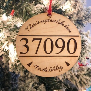 May include: A round wooden ornament with the text "There's no place like home" and the number "37090" in the center. The bottom of the ornament has the text "For the holidays" and two small pine tree illustrations.