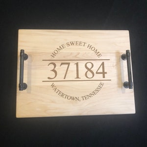 May include: A wooden serving tray with black metal handles. The tray is engraved with the text "Home Sweet Home", the number "37184", and "Watertown, Tennessee".