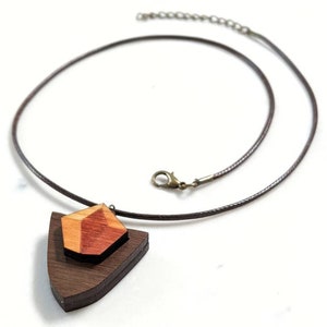 May include: A wooden pendant necklace with a geometric shape made of different shades of wood. The pendant is attached to a brown cord necklace.