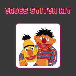 May include: A cross stitch kit featuring a colorful illustration of two cartoon characters, one yellow and one orange, with the text "CROSS STITCH KIT" above the image.
