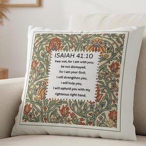 May include: Square cushion with a floral pattern and text from Isaiah 41:10. The cushion has a cream background, a decorative border, and a central text block with orange, green, and brown floral designs.