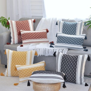 May include: A collection of decorative throw pillows with geometric patterns in various colors, including red, blue, yellow, and black. The pillows are arranged on a white couch with a white throw blanket.