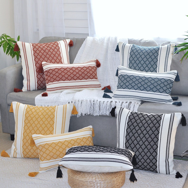 May include: A collection of decorative throw pillows with geometric patterns in various colors, including red, blue, yellow, and black. The pillows are arranged on a white couch with a white throw blanket.