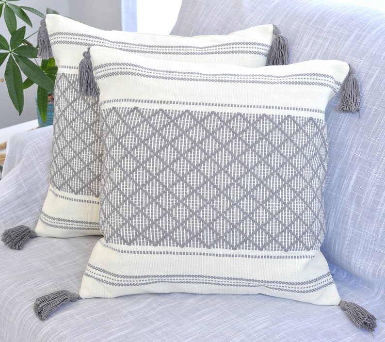 May include: Two decorative throw pillows with a white background and gray diamond pattern. The pillows have gray tassels on each corner.