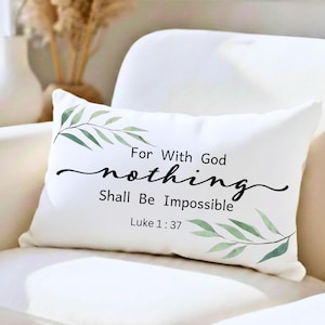 May include: White rectangular cushion with the text "For With God nothing Shall Be Impossible Luke 1:37" in black script. The cushion features green leaf accents on the corners. The cushion is placed on a white sofa.