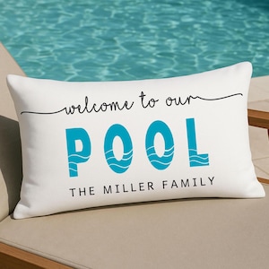 May include: White rectangular pillow with the words "welcome to our POOL" in black and turquoise. The word "POOL" has a wave design. Below the text is "THE MILLER FAMILY" in black.