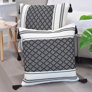 May include: Two black and white patterned throw pillows with tassels. The pillows are made of a woven fabric with a geometric design.