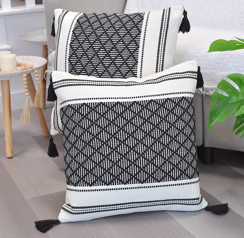 May include: Two black and white patterned throw pillows with tassels. The pillows are made of a woven fabric with a geometric design.