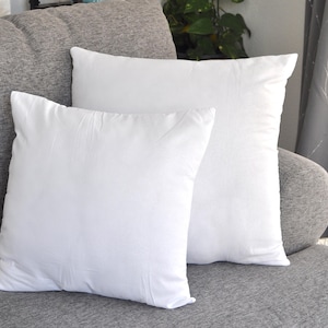 May include: Two white pillowcases on a gray couch. The pillowcases are made of a soft, smooth fabric.
