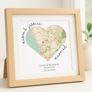 May include: A framed print featuring a heart-shaped map of a coastal area, with the names "mason & jessica" and the word "married" in script. The text "Church of the Nativity Santa Fe CA 08.26.2023" is also visible. The frame is light wood.
