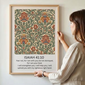 May include: A framed print featuring a floral pattern in shades of red, orange, yellow, and green on a cream background. The text "ISAIAH 41:10" and a Bible verse are printed below the pattern. The frame is a light brown color.