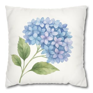 May include: A square white throw pillow featuring a centered watercolor illustration of a hydrangea flower cluster. The hydrangea displays shades of blue and light purple petals, accompanied by two green leaves on a thin stem against the white background.