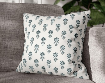 May include: A white cushion with a repeating pattern of dark blue stylised flowers. The cushion is on a grey sofa.