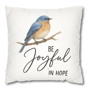 May include: White throw pillow with a watercolor painting of a bluebird perched on a branch. The text "Be Joyful in Hope" is written in black cursive script.