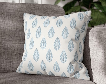 May include: A white cushion with a blue and white paisley pattern. The cushion is sitting on a grey sofa.