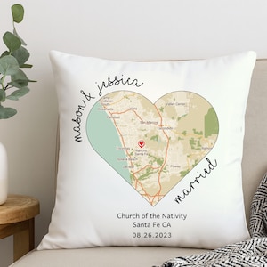Puede incluir: Cojín blanco con un diseño de mapa en forma de corazón. El mapa muestra el área de Santa Fe, CA. Los nombres "mason & jessica" y "married" están escritos en el cojín. También se incluye el texto "Church of the Nativity Santa Fe CA 08.26.2023".