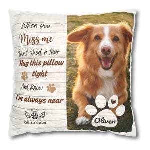 May include: White memorial pillow with a brown wooden background and a photo of a golden retriever dog. The text reads "When you Miss me Don't shed a tear Hug this pillow tight And know I'm always near" with a paw print and angel wings. The date "09.13.2024" is printed below the text. A large paw print with a heart in the center is printed below the photo with the name "Oliver" printed inside the paw print.