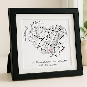 May include: A framed black and white map print in a heart shape, featuring a New York City map with a red marker. The print includes the names "mason & jessica" and the word "engaged". The text "St. Thomas Church, Manhattan NY EST. 03.15.2025" is also visible.