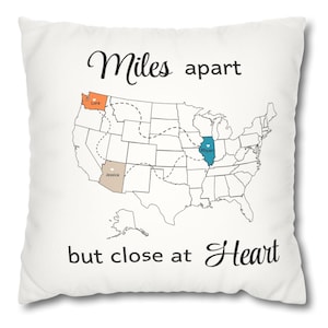 May include: White square pillow with a map of the United States, featuring the text "Miles apart but close at Heart." The map highlights three states with names: Lora, Jessica, and Rhyan. The pillow is a decorative item.