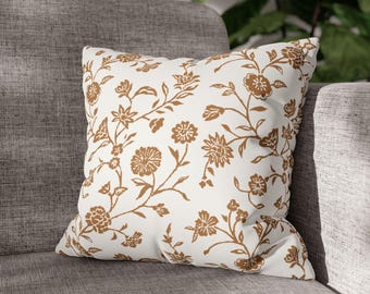 May include: A white cushion with a brown floral pattern. The cushion is sitting on a grey sofa.