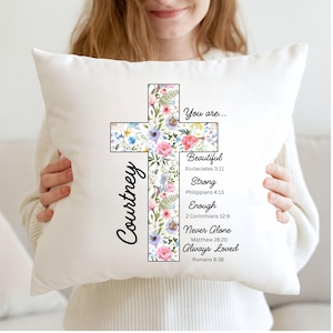 May include: White decorative pillow featuring a floral cross design with the name "Courtney" in script. The cross is filled with colorful flowers and text that reads "You are... Beautiful, Strong, Enough, Never Alone, Always Loved."