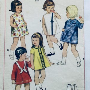 Op de afbeelding: Een vintage naaipatroon voor kinderjurken. Het patroon bevat vijf verschillende jurkstijlen, met verschillende kleuren en patronen. Het patroon is voor maten 3-6 jaar.