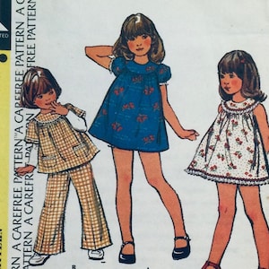 Puede incluir: Un patrón de costura vintage que presenta tres diseños de vestidos diferentes para niñas. El patrón incluye un vestido azul con estampado floral, un vestido blanco con estampado floral y un vestido a cuadros con un pantalón a juego. El patrón está etiquetado como "Carefree Pattern" y "Carefree Pattern A".