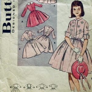 Puede incluir: Patrón de costura vintage con diseños de vestidos. El patrón incluye ilustraciones de vestidos con diferentes largos de manga y estilos de falda. La imagen principal muestra a una mujer con un vestido a rayas sosteniendo un sombrero. El patrón está etiquetado como "Butterick Designed".