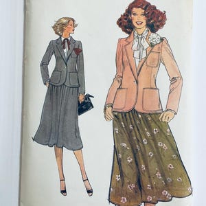 Può includere: Due donne che indossano blazer e gonne. La donna a sinistra indossa un blazer grigio e una gonna grigia. La donna a destra indossa un blazer rosa e una gonna floreale.