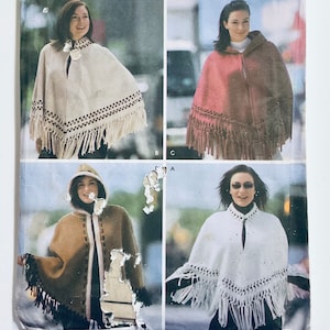 May include: Four different styles of ponchos with fringe trim. The ponchos are in white, brown, pink, and cream. Each poncho has a different pattern of stitching.