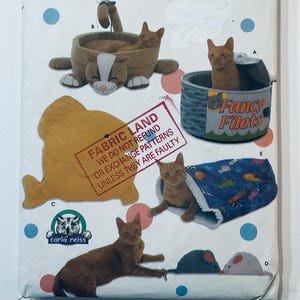 Può includere: Un foglio di modelli con disegni a tema gatto. I disegni includono una cuccia per gatti, un giocattolo per gatti a forma di pesce, un gatto in una lattina con l'etichetta "Fancy Filets" e un gatto in un letto a tunnel. Il testo "Fabric Land" è incluso.