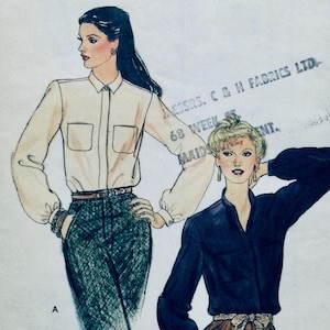 Op de afbeelding: Twee blouses voor vrouwen, een witte met een knoopsluiting en de andere donkerblauw met een V-hals. Beide blouses hebben lange mouwen en zijn in een broek gestopt.