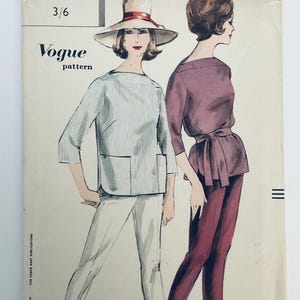 May include: A vintage Vogue pattern envelope featuring an illustration of two outfits. One figure wears a light blue pinstriped top with pockets and white trousers, while the other wears a solid plum-coloured top with a waist tie and matching trousers.