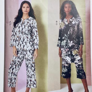 May include: Two women modeling floral print outfits. One outfit is white with black and brown floral patterns, the other is black with white and gold floral patterns. Both outfits include a long-sleeved top and matching pants.
