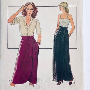 May include: Vintage sewing pattern with illustrations of two women's fashion designs. One design shows a wrap skirt in burgundy with a cream blouse. The other design is a long black skirt with a white top.