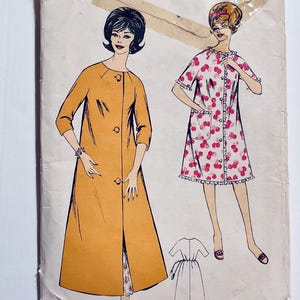 May include: A vintage sewing pattern with illustrations of two women's garments. One is a long, mustard-coloured coat with large buttons. The other is a short, white dress with a red cherry print. A smaller dress illustration is also included.