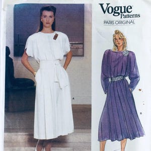 May include: Vogue Patterns Paris Original sewing pattern featuring two women's dresses. The first dress is white with a sash and the second dress is purple with a silver belt. The pattern is labeled "Vogue Patterns Paris Original".