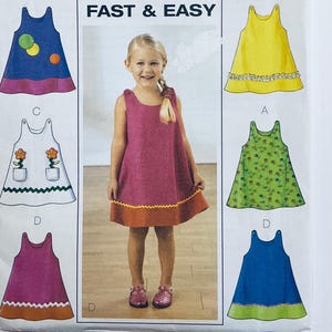 May include: A sewing pattern featuring a young girl wearing a pink dress with an orange hem. The pattern shows several dress designs in blue, yellow, green, and pink, with various details. The text "FAST & EASY" is at the top.