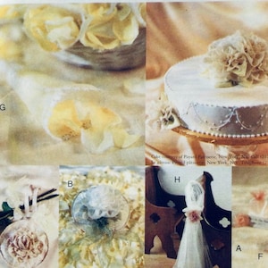 Könnte beinhalten: Eine weiße Hochzeitstorte mit einer weißen Zuckerblume obenauf. Die Torte ist mit einem silbernen Design verziert und steht auf einem silbernen Tortenständer. Die Torte ist von weißen Blumen umgeben.