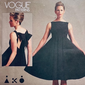 May include: Vogue Patterns dressmaking pattern featuring a black dress with a bow detail on the back. The pattern includes a side view of the dress and the words "VOGUE PATTERNS" at the top.