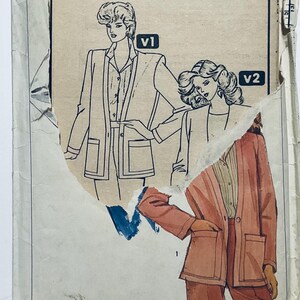 Könnte beinhalten: Eine Schnittmusterhülle mit Abbildungen von zwei Blazer- und Hosen-Outfits, beschriftet mit V1 und V2. Die Hülle ist zerrissen und gibt den Blick auf eine teilweise farbige Illustration eines pfirsichfarbenen Blazer-Hosen-Sets frei.