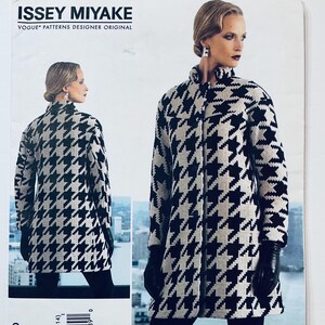 Puede incluir: Un original de diseñador de Vogue Patterns de Issey Miyake. La imagen muestra a una mujer con un abrigo de pata de gallo en blanco y negro con cuello alto y mangas largas. El abrigo llega a la rodilla y tiene un diseño clásico y entallado.