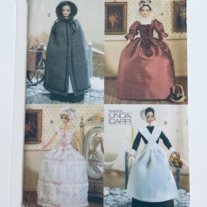 May include: A vintage sewing pattern for making doll clothes. The pattern includes four different designs: a grey hooded cape, a burgundy gown, a white dress with lace trim, and a white apron with a black bodice. The pattern is designed by Linda Carr.