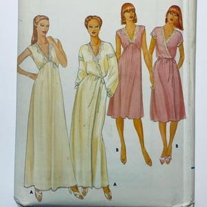 Puede incluir: Un sobre de patrón de costura con ilustraciones de cuatro prendas. Dos vestidos largos en color crema y dos vestidos hasta la rodilla en rosa, todos con escote en V, adornos de encaje y lazos en la cintura. El patrón está marcado con A y B.